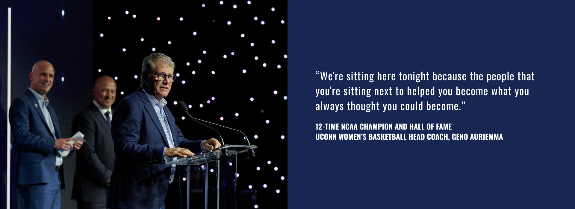 "We're sitting here tonight because the people that you're sitting next to helped you become what you always thought you could become." 12-Time NCAA Champion and Hall of Fame UConn Women's Basketball Head Coach, Geno Auriemma next to a man standing at a podium, speaking into a microphone against a background of twinkling lights.